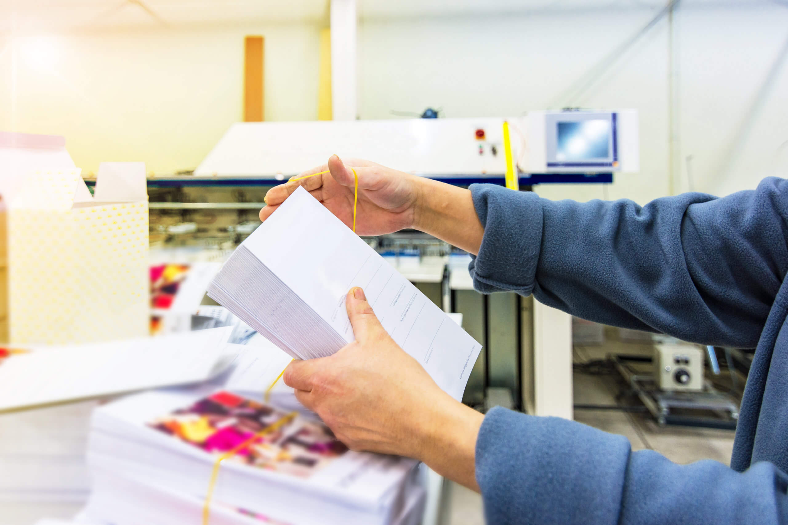 Hands holding a stack of printed materials in a printing facility, showcasing quality control in digital printing services for brochures and marketing materials.