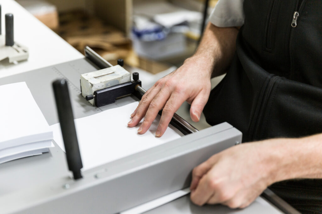 Hands operating a paper cutter in a printing facility, preparing construction drawings and blueprint copies for clients in Chalfont.
